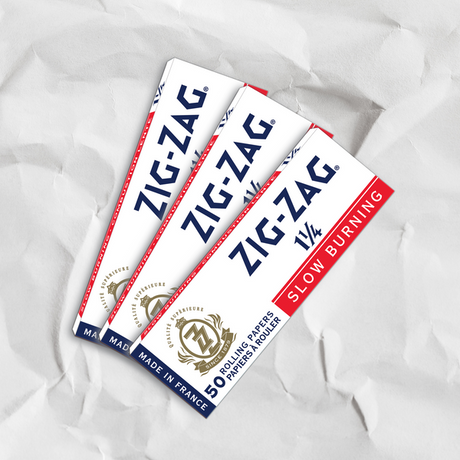 Zig-Zag 1 1/4 White Rolling Paper displayed on crumpled paper, highlighting their thin, easy-to-roll sheets and slow-burning quality.