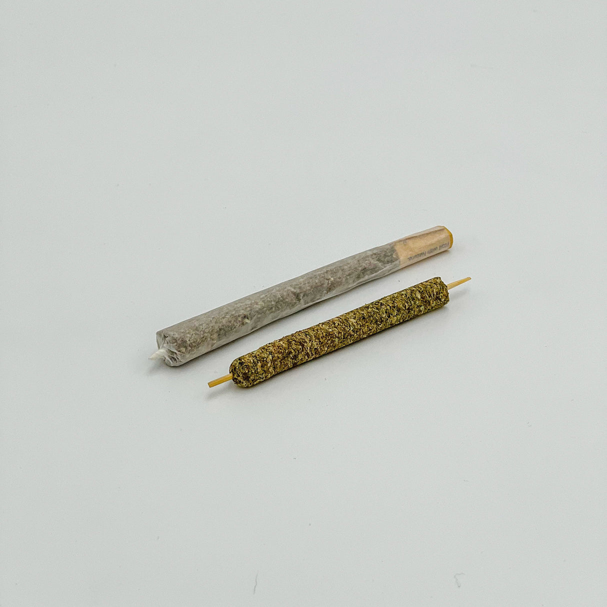 Close-up of Mini CannaMold, a tool for crafting slow-burning cannagars with built-in airflow, shown beside a rolled joint and cigarette for comparison.