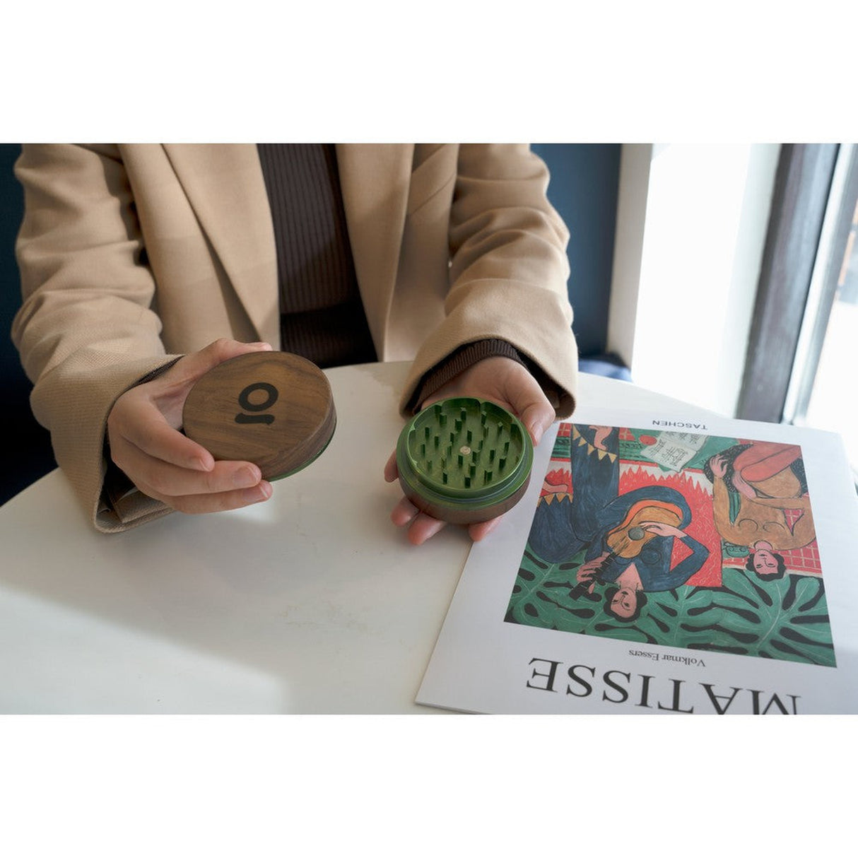 Person holding the 2pcs Metal 3 Magnetic Grinder, showcasing its round design and grinder teeth, over a book.