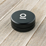 Aluminum Storage Puck, a compact, black round container with a white letter, ideal for discreet, airtight storage, shown on a wooden surface.