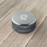 Aluminum Storage Puck on a wooden surface, featuring a discreet silver design with a white logo, ideal for compact, airtight storage with a durable, interchangeable seal.