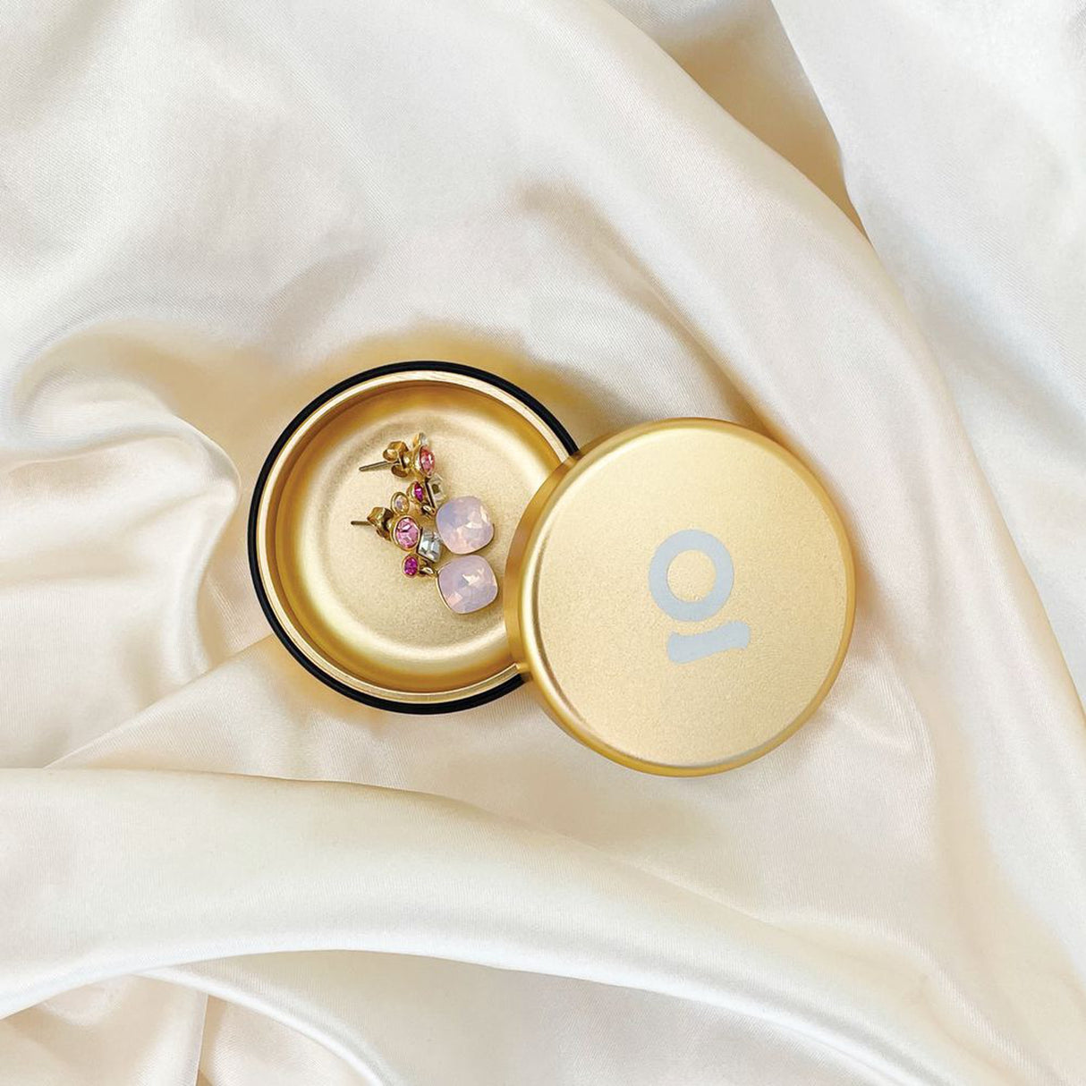 Gold, round Aluminum Storage Puck containing earrings, showcasing its compact, durable design for discreet, on-the-go storage with an airtight seal.