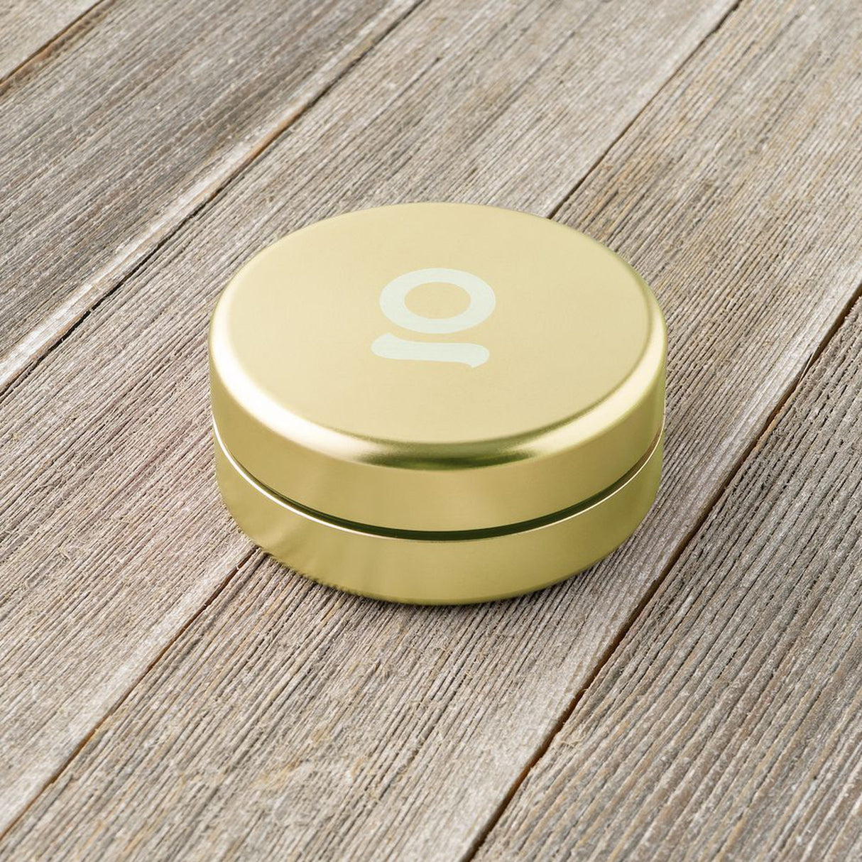 Aluminum Storage Puck on a wooden surface, featuring a white logo. Compact and airtight, ideal for discreet storage of small items.