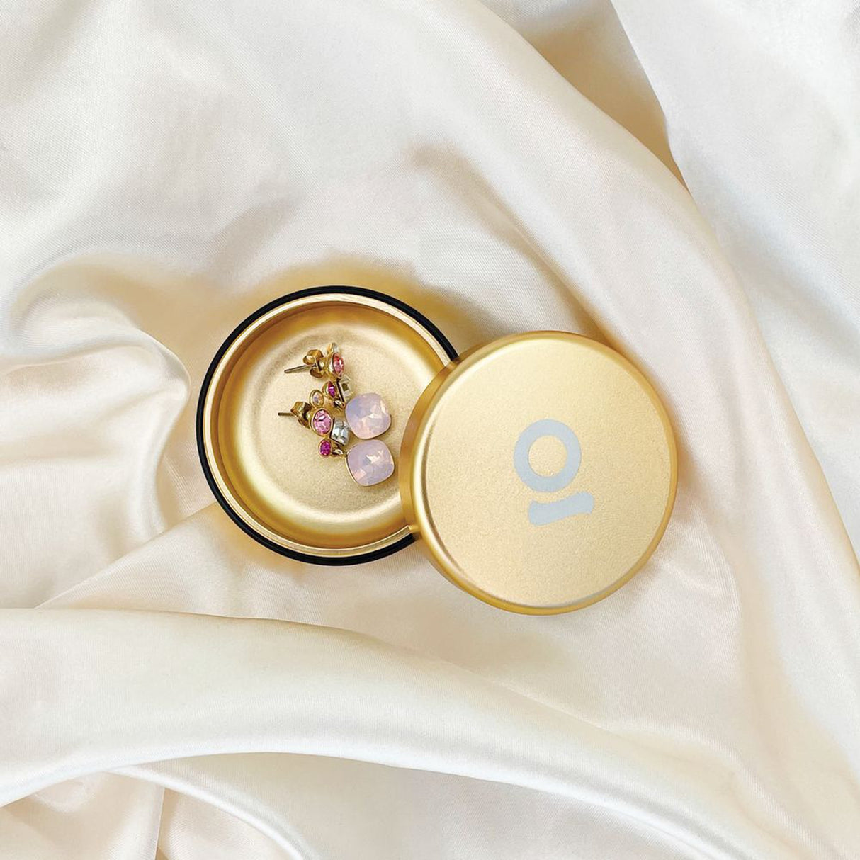 Aluminum Storage Puck with gold finish, containing earrings, designed for discreet on-the-go storage, featuring an airtight rubber seal for odor containment.