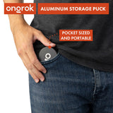 A person places a pocket-sized Aluminum Storage Puck into their jeans pocket, illustrating its portability and discreet design for on-the-go item storage.