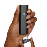 Hand holding the PAX Plus Dry Herb Vaporizer, a sleek black electronic device, showcasing its compact and ergonomic design for convenient portable vaping.