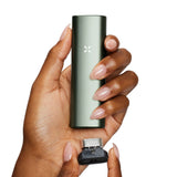 Hand holding PAX Plus Dry Herb Vaporizer, highlighting its compact design and dual-use functionality, ideal for on-the-go vaping enthusiasts.