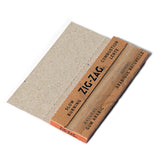 Close-up of a cardboard box containing Zig-Zag 1 1/4 Unbleached Rolling Papers, emphasizing their natural, unbleached fibers and ultra-thin, slow-burning design.