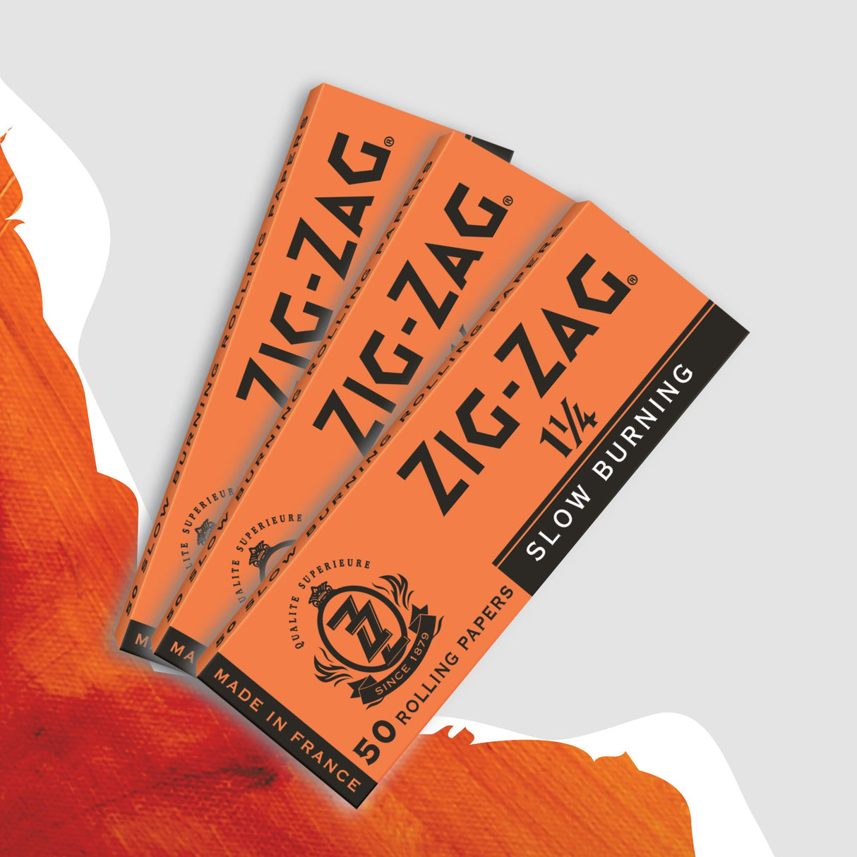 Close-up of Zig-Zag 1 1/4 Orange Rolling Paper pack, featuring black and orange logos, highlighting its premium, slow-burning papers made from natural flax fibers.