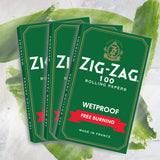 Stack of Single Wide Green Rolling Paper featuring a green and gold logo, highlighting Zig-Zag's wetproof, thick design for a smooth, slow burn.